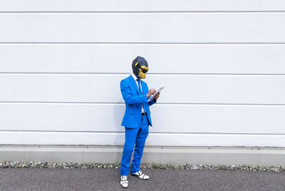 Full length of man using mobile phone against wall