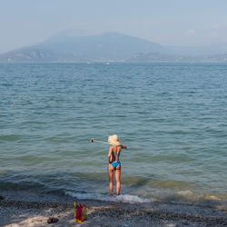 Rear view of woman wearing bikini taking selfie at beach