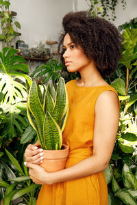 Young woman looking away while standing against plants