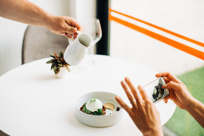 Hands taking photos of food with smartphone while waiter serving meal