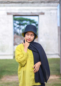 Young woman looking away while standing against wall