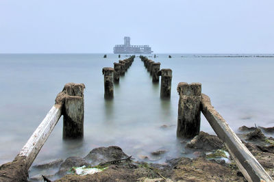 Wooden posts in sea against clear sky