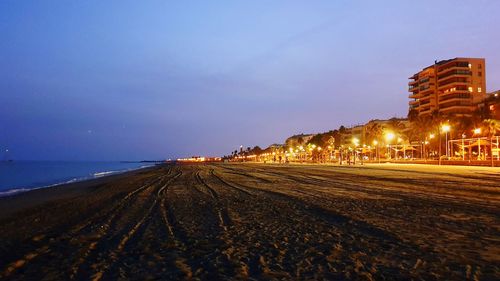 Illuminated street by sea against sky at night