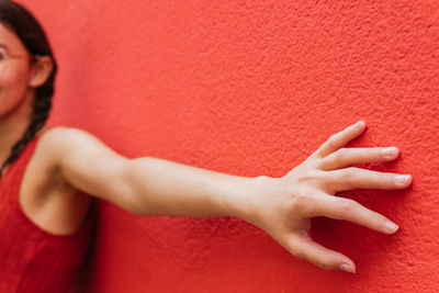 Side view of cropped unrecognizable female leaning on red wall of building in street with outstretched arm