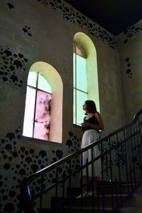 Man looking through window while sitting on staircase in building