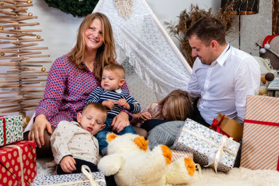 Happy family sit between christmas gift boxes and toys in a decorated house