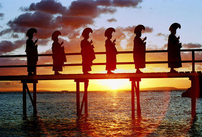 Silhouette people standing on pier over sea against sky during sunset