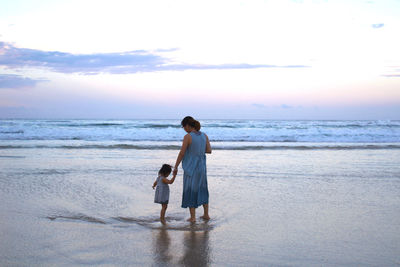 Rear view of siblings on beach against sky