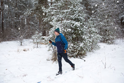 Skier with a backpack and hat with pompom with ski poles in his hands on background 