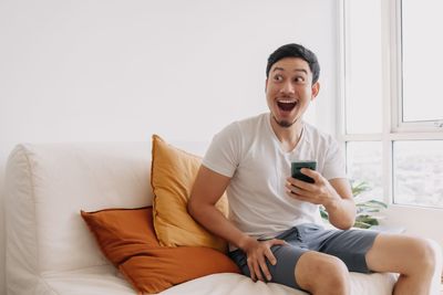 Young woman using mobile phone while sitting on bed at home