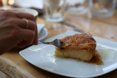 Close-up of hand in plate eating galaktoboureko 