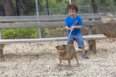 Four-year-old boy  in the park with his little brown dog next to a wooden bench, enjoying 