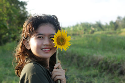 Portrait of smiling woman with yellow flower in field