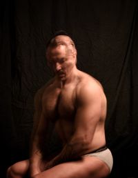 Midsection of shirtless man standing against black background