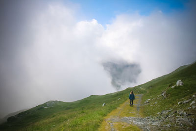 Rear view of woman walking on mountain against cloudy sky