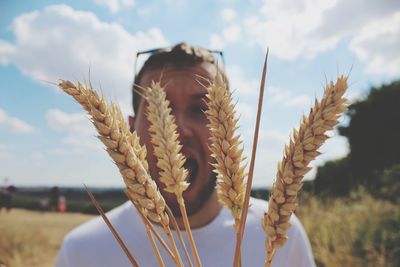 Close-up of shocked man with wheat crops at farm against sky