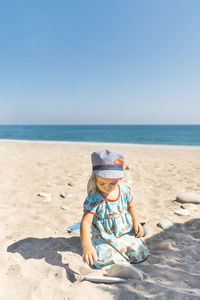 Boy sitting on beach by sea against clear sky