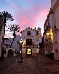 Street amidst buildings against sky at sunset