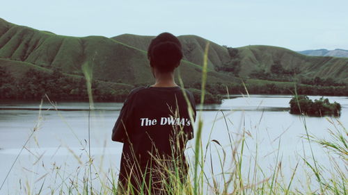 Rear view of woman standing by lake against mountain