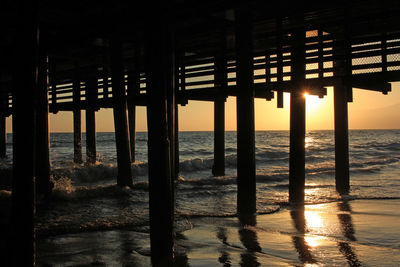 Silhouette pier on beach against sky during sunset