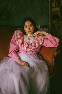 Portrait of young woman sitting on pink indoors