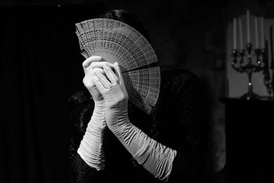 Woman face covered with hand fan in darkroom