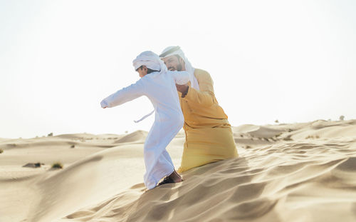 Rear view of friends on sand at beach against sky