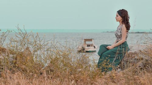 Young woman sitting on shore at beach against sky