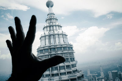 Cropped hand gesturing against petronas tower in city