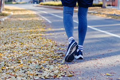 Close-up of male feet in trainers going to run on the street with yellow leaves on the ground. 