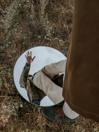 A guy in a brown raincoat is reflected in a round mirror that lies on the grass