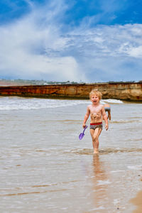 Full length of young woman standing in sea against sky