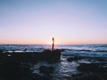 Woman standing on rock against sea during sunset
