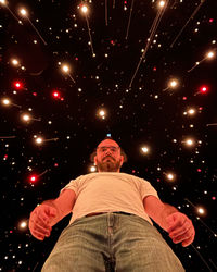 Portrait of woman sitting on illuminated string lights at night