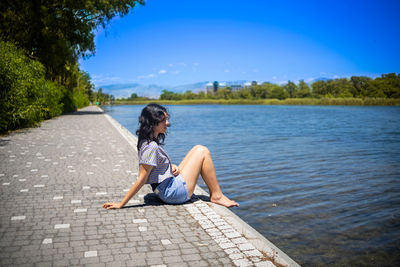 Full length of woman standing by lake against clear sky