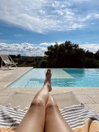 Low section of woman relaxing at pool against sky