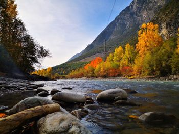 Stream flowing through rocks by river against sky during autumn