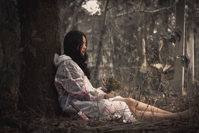 Full length of woman sitting on tree trunk in forest