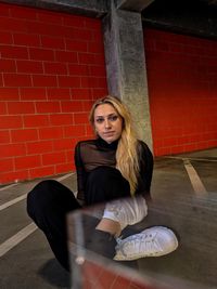 Portrait of young woman sitting against brick wall