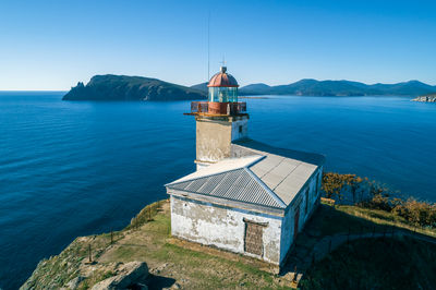 Lighthouse by sea against clear blue sky