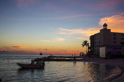 Silhouette people on sea against sky during sunset