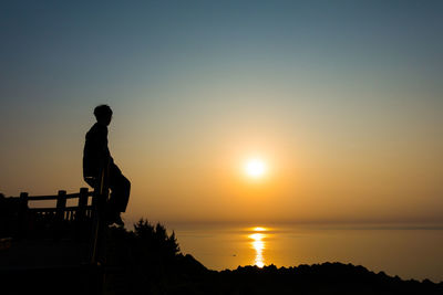 Silhouette man standing by sea against clear sky during sunset