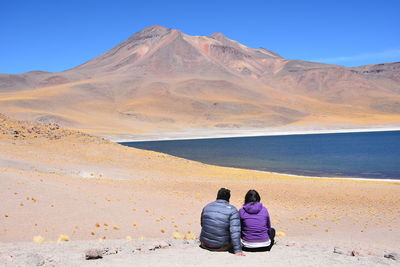 Rear view of people sitting on desert against mountain