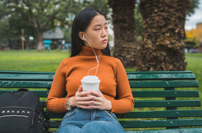 Young woman looking away while sitting on bench in park