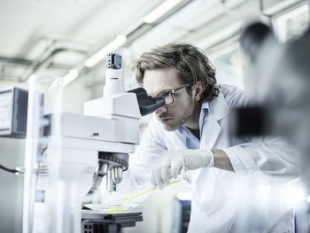 Laboratory technician looking through microscope in lab