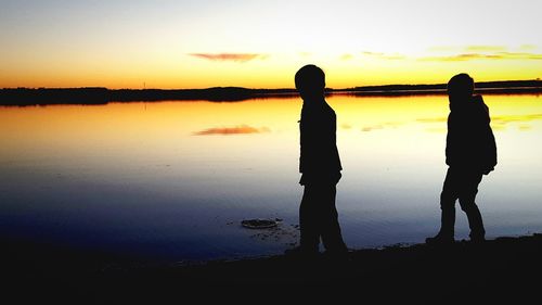 Silhouette people standing by lake against sky during sunset