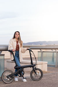 Vertical view of woman happy and smiling holding an electric bike in the city with copy space