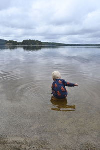 Rear view of men sitting in lake against sky