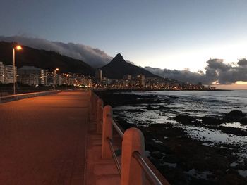 Illuminated city by sea against sky