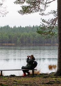 Rear view of woman sitting on bench against lake